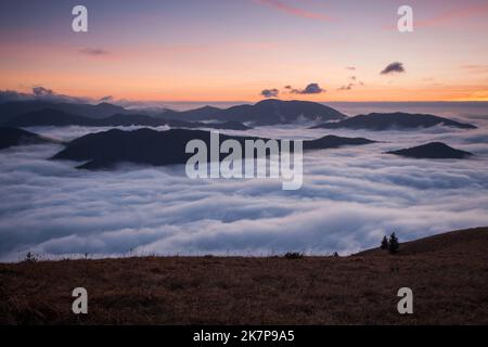 Sunset hidden behind clouds and fog over hills, bright yellow sun on colorful cloudscape, blue violet orange sky. Stock Photo