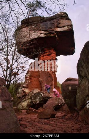 Hinterweidenthal, Germany - January 1, 2021: Two children climbing on red rocks under the rock formation called Devil's Table in the Palatinate Forest Stock Photo