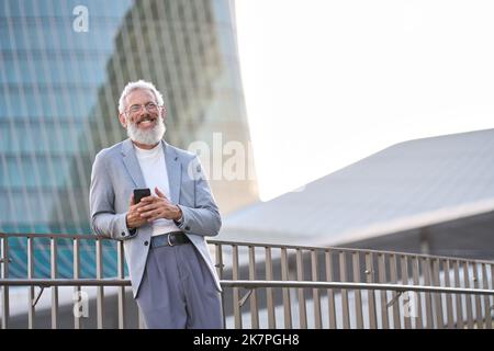 Happy old professional business man holding smartphone using cell phone outside. Stock Photo