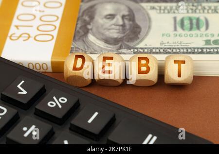 Business concept. On a brown surface are dollars, a calculator and wooden cubes with the inscription - DEBT Stock Photo