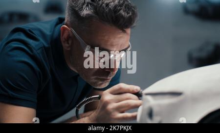 Senior automotive design engineer uses a rotary tool for perfecting the rake sculpture of a car model in a high tech company. Engineer wearing safety goggles works in an automotive company. Stock Photo