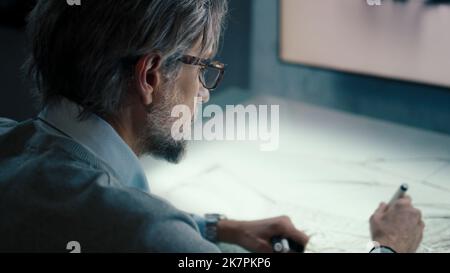 Senior automotive graphic designer with black framed glasses and beard works in a high tech innovative laboratory. Draws sketch of the prototype model of a car render. Stock Photo