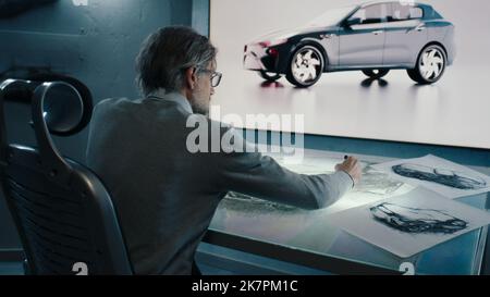 Automotive graphic designer draws sketch of the prototype model of a car with digital display graphics touch sreen table, using stylus pen in a high tech innovative laboratory. Stock Photo