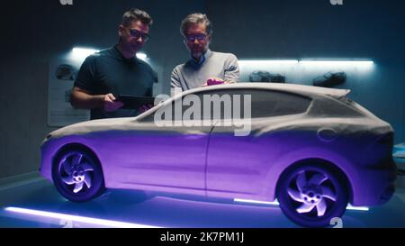 Experienced automotive engineers examine the prototype car model using different colors of light to make final design changes. Using a digital touchscreen tablet in a hightech car manufacturing company. Stock Photo