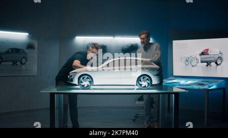 Experienced automotive engineers discuss the design infront of a rake sculpture prototype car model. Engineers use a touch screen digital tablet in a high tech laboratory. Make design corrections. Stock Photo