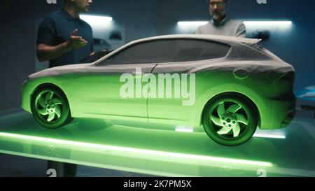 Experienced automotive engineers examine the prototype car model in different shades of light to choose color of future car. Using special App on digital tablet and lighting table. Stock Photo