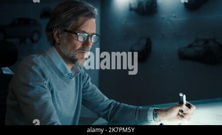 Senior automotive graphic designer with black framed glasses and beard works in a high tech innovative laboratory. Draws sketch of the prototype model of a car render. Stock Photo