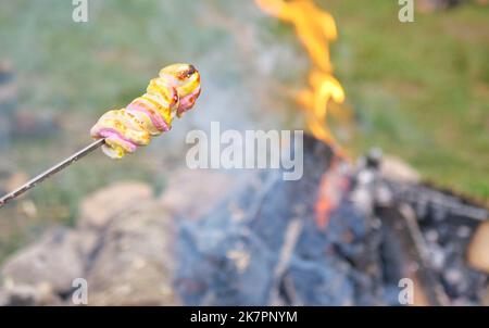 Close-up video of food being grilled over a campfire near a tent at a campsite. Focus on the fire. Marshmallow on fire Stock Photo