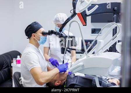 Dentist and assistant check patient's teeth with dental tools - microscope, mirror and probe in dental clinic office. Concept of medicine, dentistry a Stock Photo