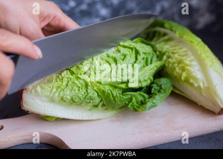 girl cook cuts a vegetable chinese cabbage leaves romaine lettuce on a wooden board in the kitchen Stock Photo