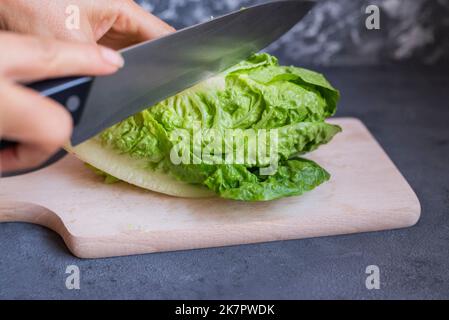 girl cook cuts a vegetable chinese cabbage leaves romaine lettuce on a wooden board in the kitchen Stock Photo