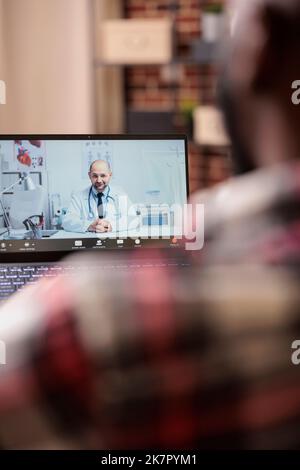 Young adult talking to doctor on videocall, using remote telemedicine videoconference with medic. Chatting about healthcare at online telehealth appointment, teleconference call. Stock Photo