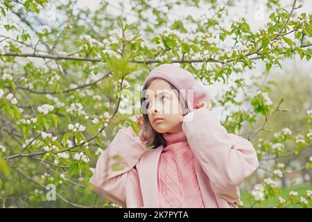 little girl stands in a blooming white apple tree in the park. Stock Photo