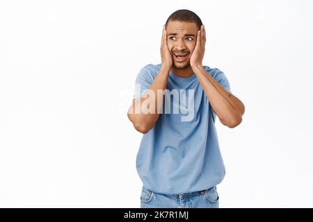 Portrait of scared and worried arab man, holds hands on head and looking in panic at camera, standing over white background Stock Photo