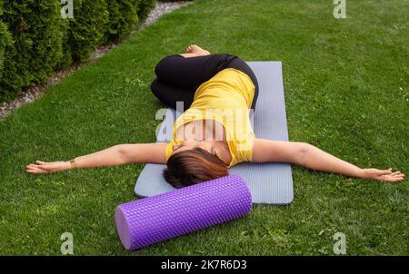 Woman learning to pratice yoga lying on a mat doing asanas for beginners on a meadow in summer Stock Photo