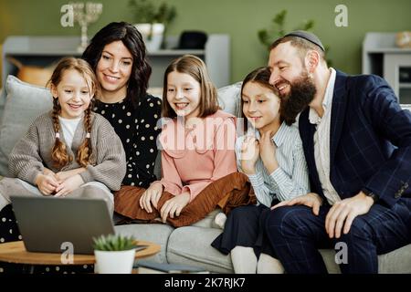 Portrait of modern jewish family using laptop and calling by video chat in cozy home setting Stock Photo