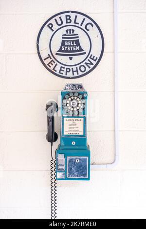 Retro bue wall payphone made by Crosley on a white wall with a Bell System Public Telephone sign above. Stock Photo