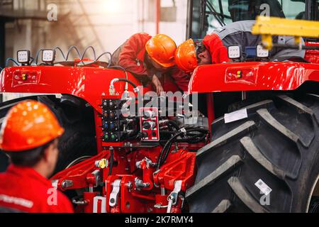Industrial workers assembles agricultural tractor in workshop. Stock Photo