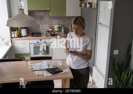 Mature lady searches phone number of hotline to solve problem about electricity bills. Family budget Stock Photo