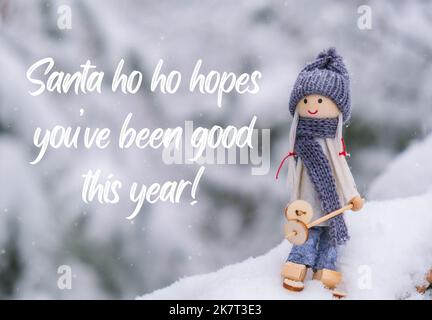 Santa ho ho hopes you have been good this year Inspiration joke quote phrase Angel gnome in scarf and knitted hat skiing on snowy fir branch Elf toy on skis in snowy landscape New year and Merry Christmas greeting card. Winter Holidays resort Stock Photo