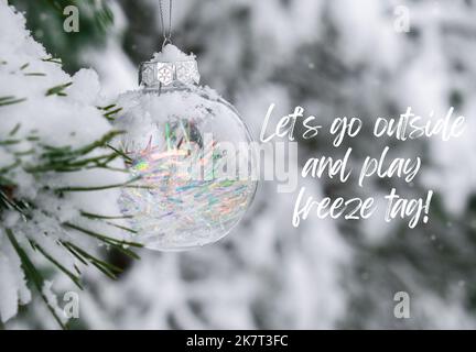Lets go outside and play freeze tag Inspiration joke quote phrase Transparent trendy glass Christmas ball on snowy branch firs in winter forest. Winter holiday background. Happy new year Merry Christmas greeting card. Snow falling in background Stock Photo