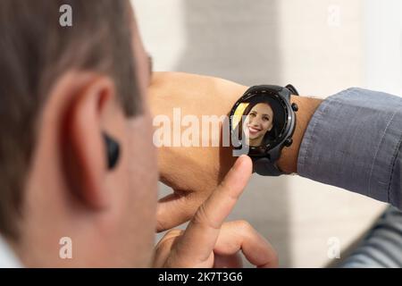 attractive man looking on watch while talking by smartphone. incoming call on a modern smart watch. the guy presses a button on his watch. Stock Photo