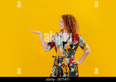 Happy confident young woman posing sideways, turning palm of her hand up. Stock Photo