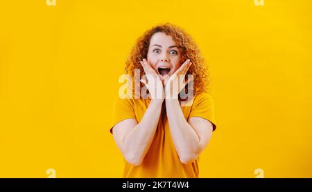 Pleasantly surprised young woman with curly hair standing with gaping mouth Stock Photo