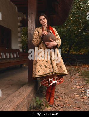 Pensive beautiful young woman dressed traditional ukrainian embroidered clothes holding old crock in her hands looking at the camera. Vintage outfit Stock Photo