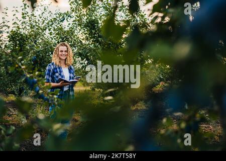 Woman agronomist specialist on the farm field holding phone and notepad to collect data quality. Agricultural business concept. Nature concept Stock Photo