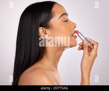 Accentuating her best features. an attractive young woman applying lipstick against a pink background. Stock Photo