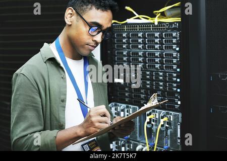 Skilled in and abled in the handling of wires and cables. a young man making notes while working in a server room. Stock Photo