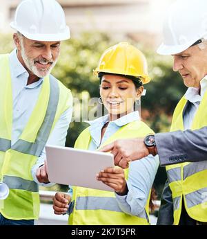 Seamless collaborations are key. a group of businesspeople using a digital tablet while working at a construction site. Stock Photo