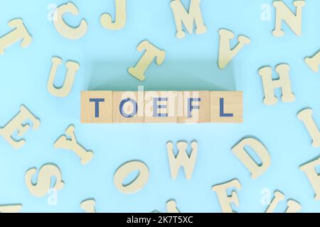 TOEFL or test of english as a foreign language testing system exam concept. Wooden blocks typography flat lay on blue background. Stock Photo