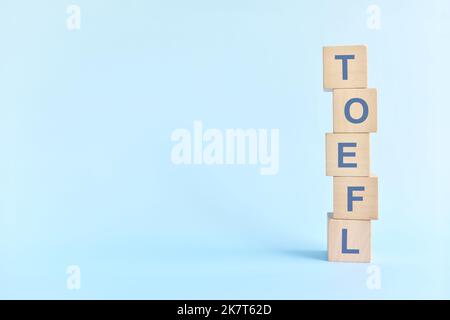 TOEFL or test of english as a foreign language testing system exam concept. Wooden blocks typography flat lay on blue background. Stock Photo