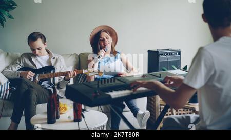 Attractive young people musical band are holding rehearsal in nice room at home, playing musical instruments and singing in microphone. Music and millennials concept. Stock Photo
