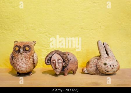 Clay figurines of animals on a yellow background close-up. Crafts from clay. Owl, ram and hare from clay. Stock Photo