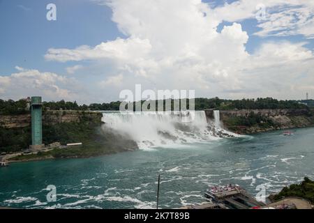 American Falls view from Canada side on cloudy day. Waterfall with blue river and rocky shore. Summer. Cruise ship with tourists Niagara falls, Stock Photo