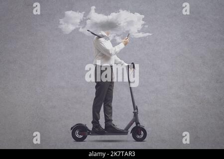 Businessman riding an electric scooter with his head in a cloud, he is using a smartphone: isolation, distraction and smartphone addiction concept Stock Photo