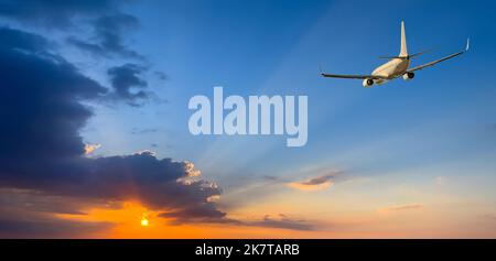 the plane in the sky is landing on the background of sunset Stock Photo