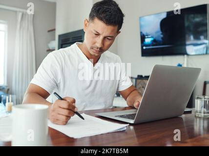 Finding his way through the figures. a handsome young man working on his laptop in the living room at home. Stock Photo