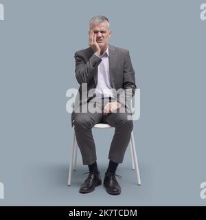 Man sitting on a chair and touching his cheek, he is having a bad toothache, dentist and dental care concept Stock Photo