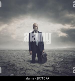 Businessman trapped in a dry desert land, he is lost and hopeless, crisis and environmental damage concept Stock Photo