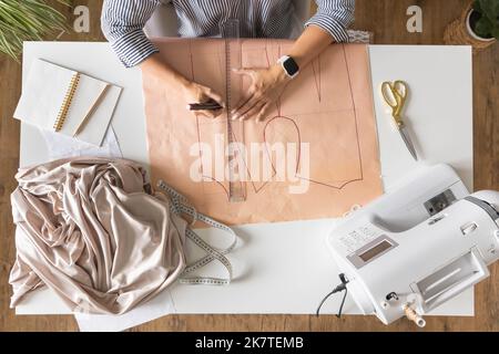 Female tailor hands draw sew pattern ruler on desk clothes creating workshop top view closeup Stock Photo
