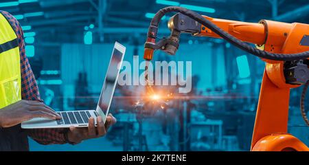 Engineer worker using laptop computer program control Robotic Arm Welding with AI automation system in advanced modern metal factory.Industry 5.0 fabr Stock Photo