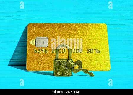 Keyed padlock in front of a golden credit card placed on a blue wooden background. Financial fraud protection concept. Stock Photo