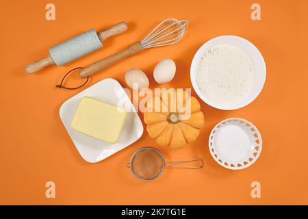 Pumpkin pie ingredients and baking tools on orange background Stock Photo