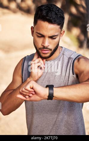 The cardio seems to be paying off. a handsome young man standing alone outside and using his watch to time his pulse after a run. Stock Photo