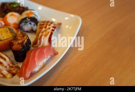 Various sushi in a white plate placed on a wooden table Stock Photo