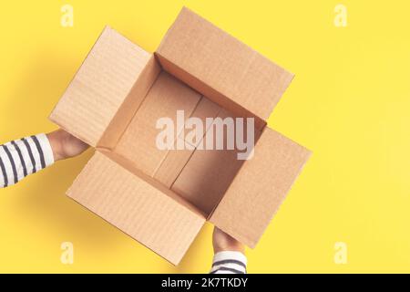 Woman hands holding empty open brown cardboard box on yellow background. Top view, copy space Stock Photo